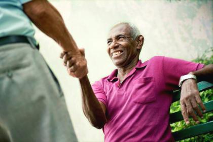 An elderly man seated on a bench shakes hands with a man standing up.